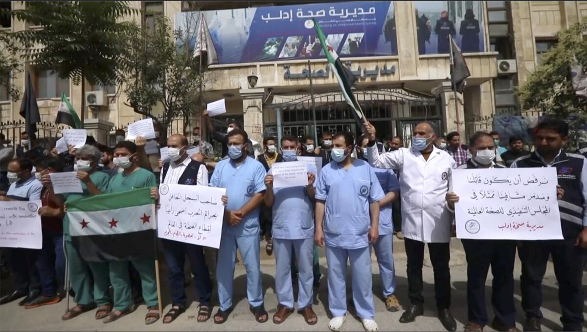 In this image taken from video, dozens of medical workers protest a decision to grant Syrian President Bashar Assad’s government a seat on the executive board of the World Health Organization, Monday, May 31, 2021, in Idlib, Syria. (AP Photo)