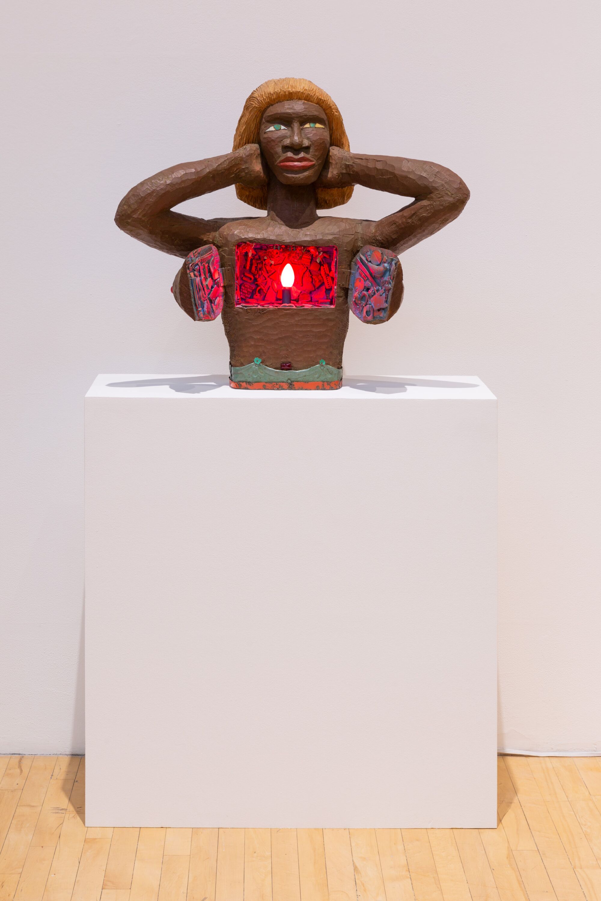 A wooden sculpture of a woman's torso opens at the chest to reveal a red illuminated light within