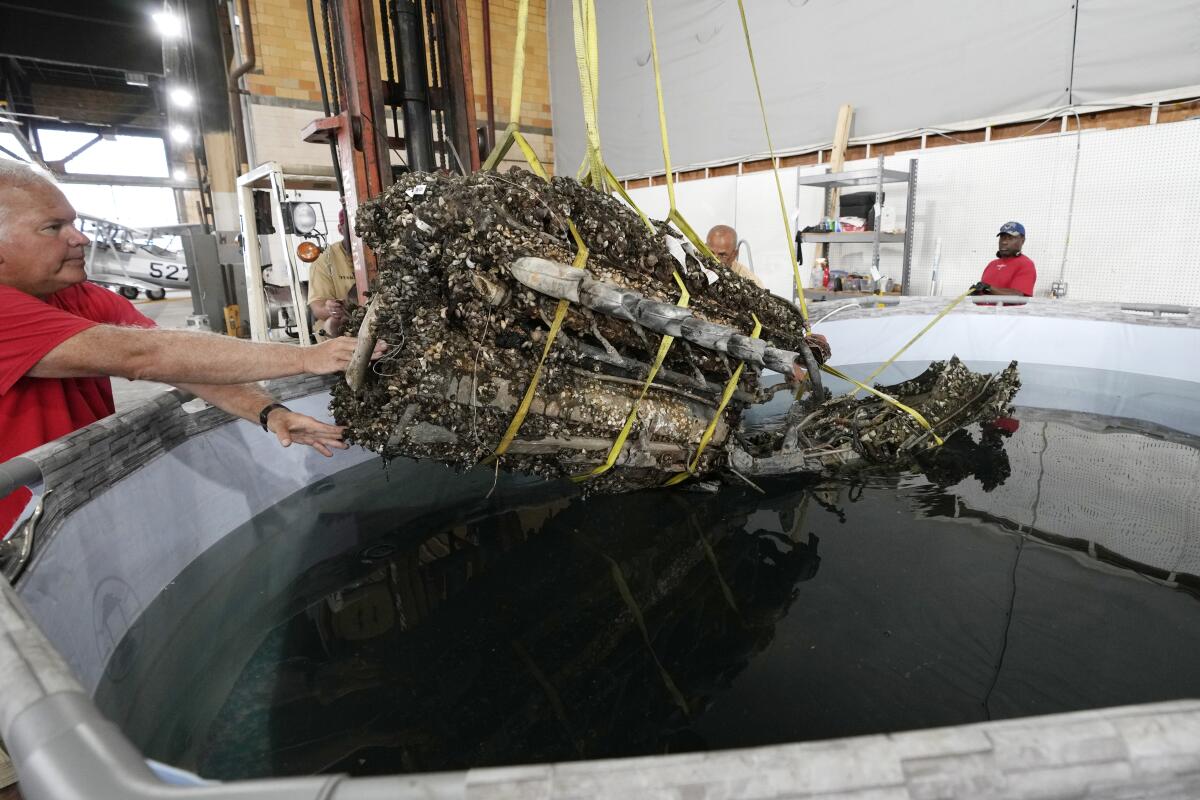 A man guides the mussel-encrusted engine from a P-39 World War II-era fighter plane into a chemical solution.
