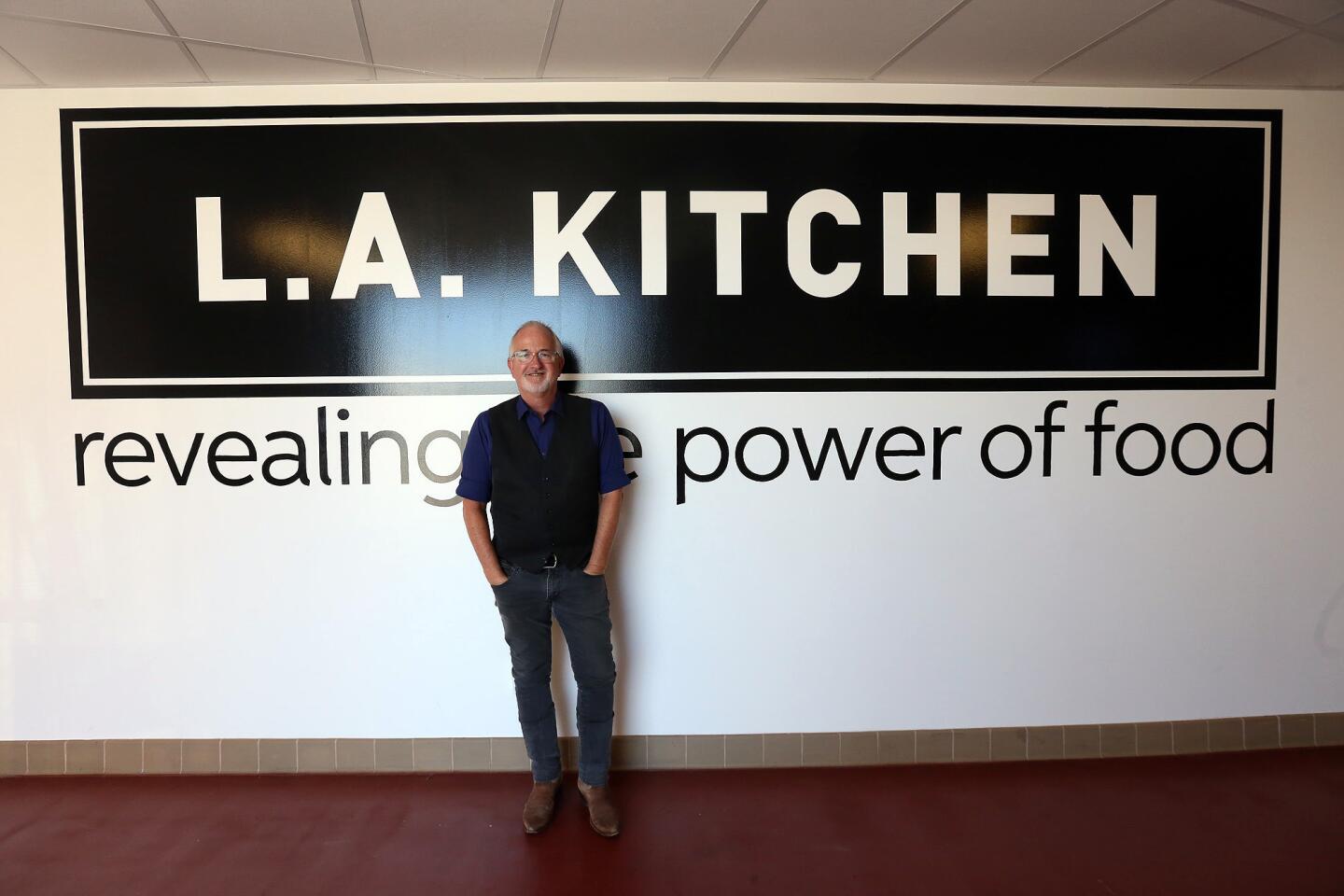 Robert Egger, president of L.A. Kitchen, stands near the company's logo. Under the leadership of Egger, L.A. Kitchen is training disadvantaged people to cook and then distribute the dishes to low-income elderly.