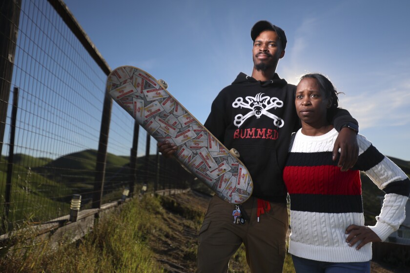 A man holds a skateboard in one hand and has his other arm on a woman's shoulders.