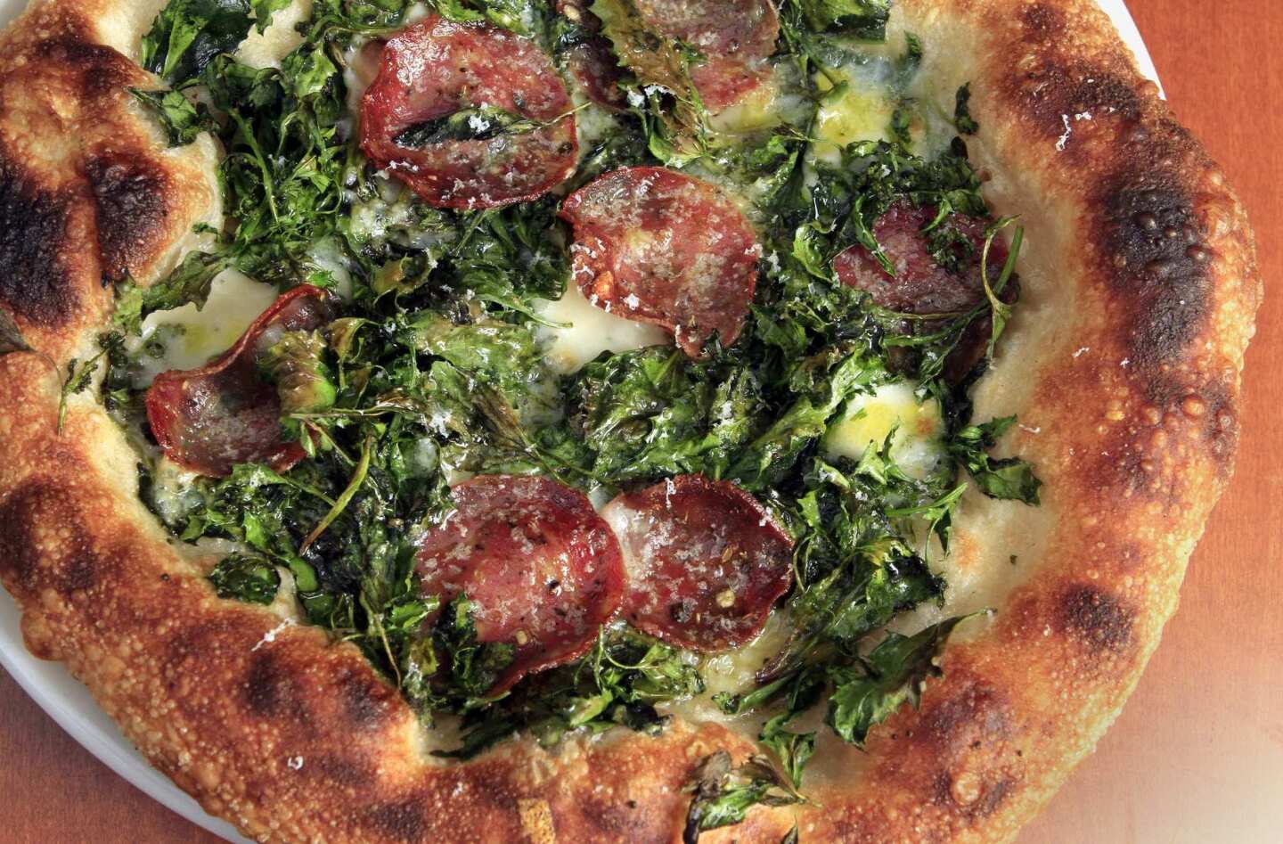 Pizza with thin slices of finocchiona salame, wild spinach and cacio di Roma cheese.