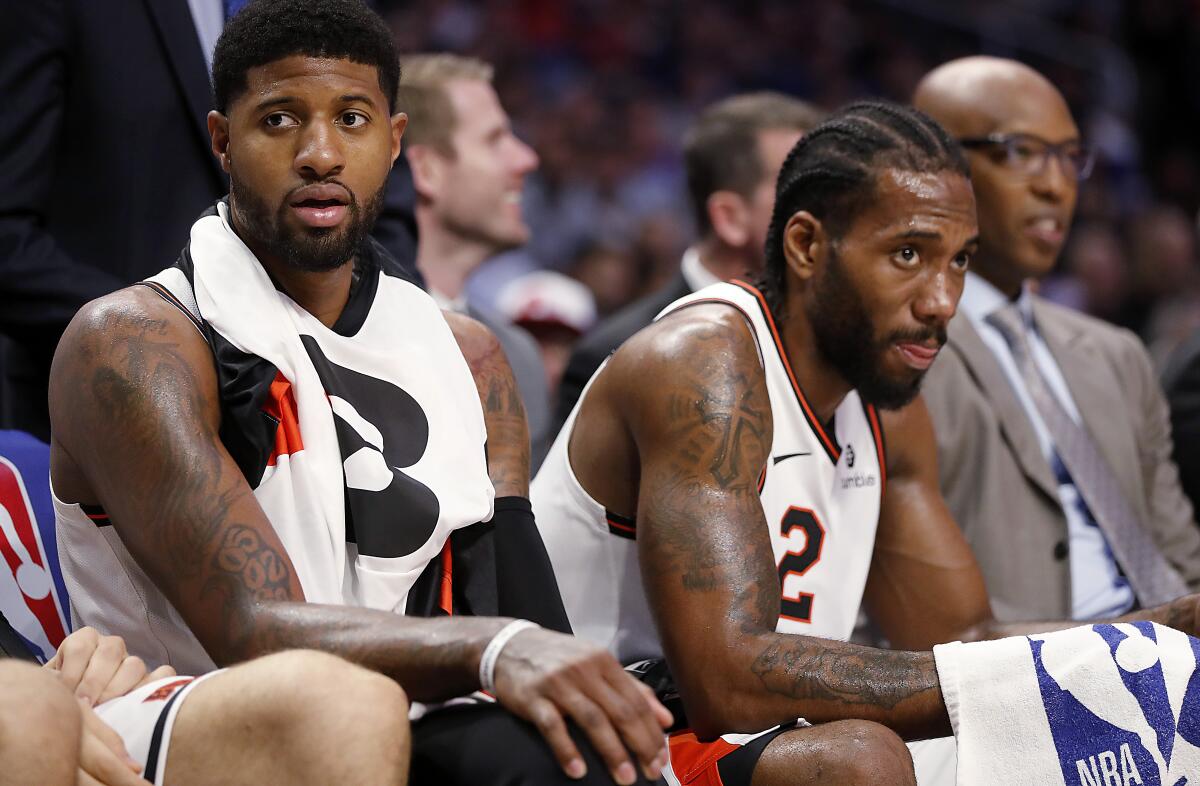 All-Star forwards Paul George, left, and Kawhi Leonard watch a game from the bench on Dec. 3, 2019.