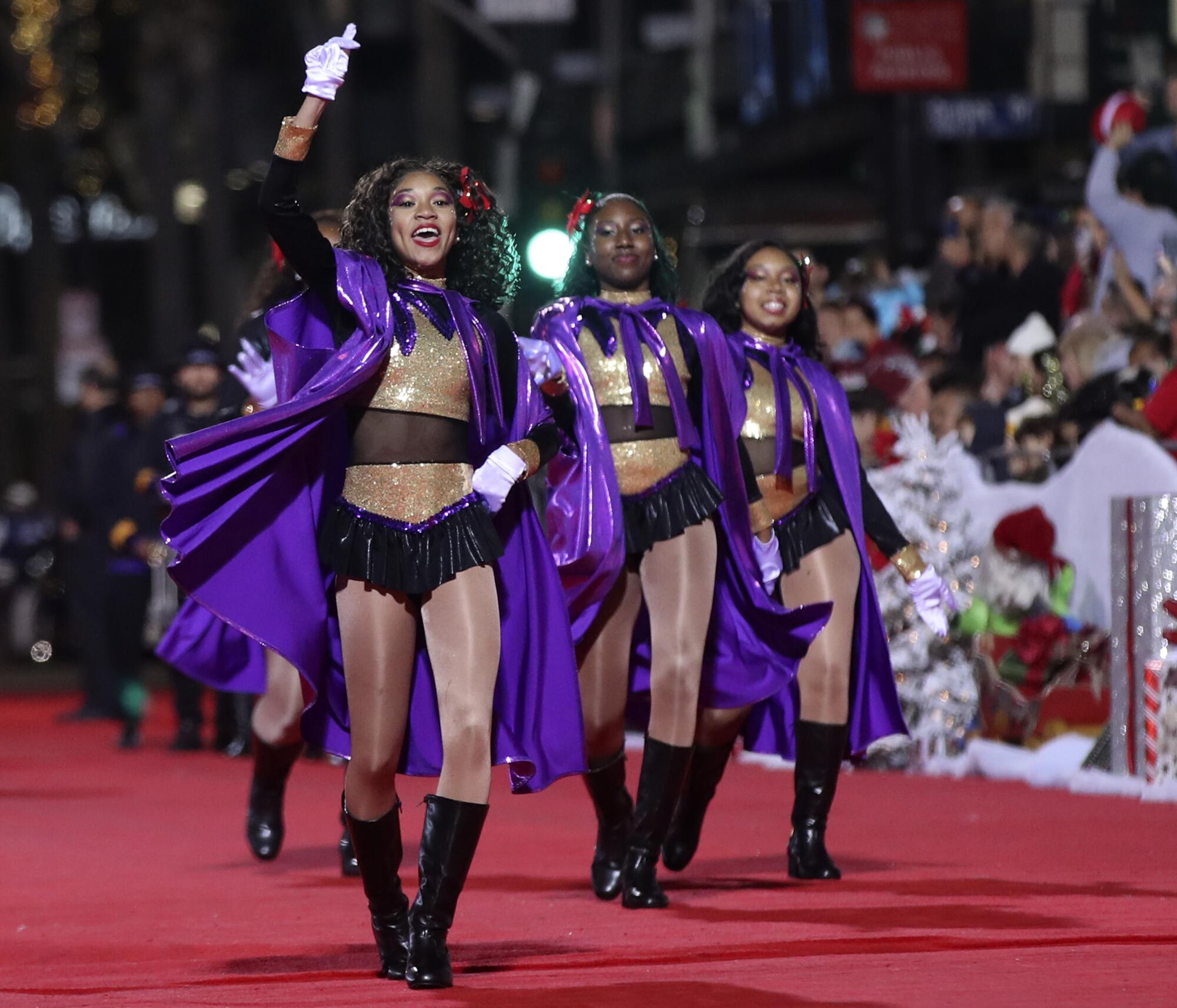 Women in purple, gold and black costumes perform on the red carpet.