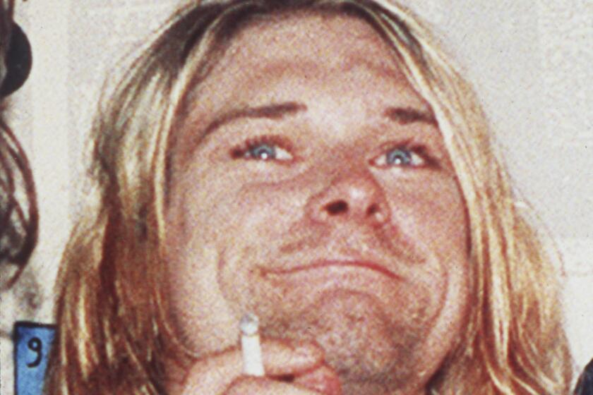 A photo of a shaggy-haired man smiling and smoking a cigarette