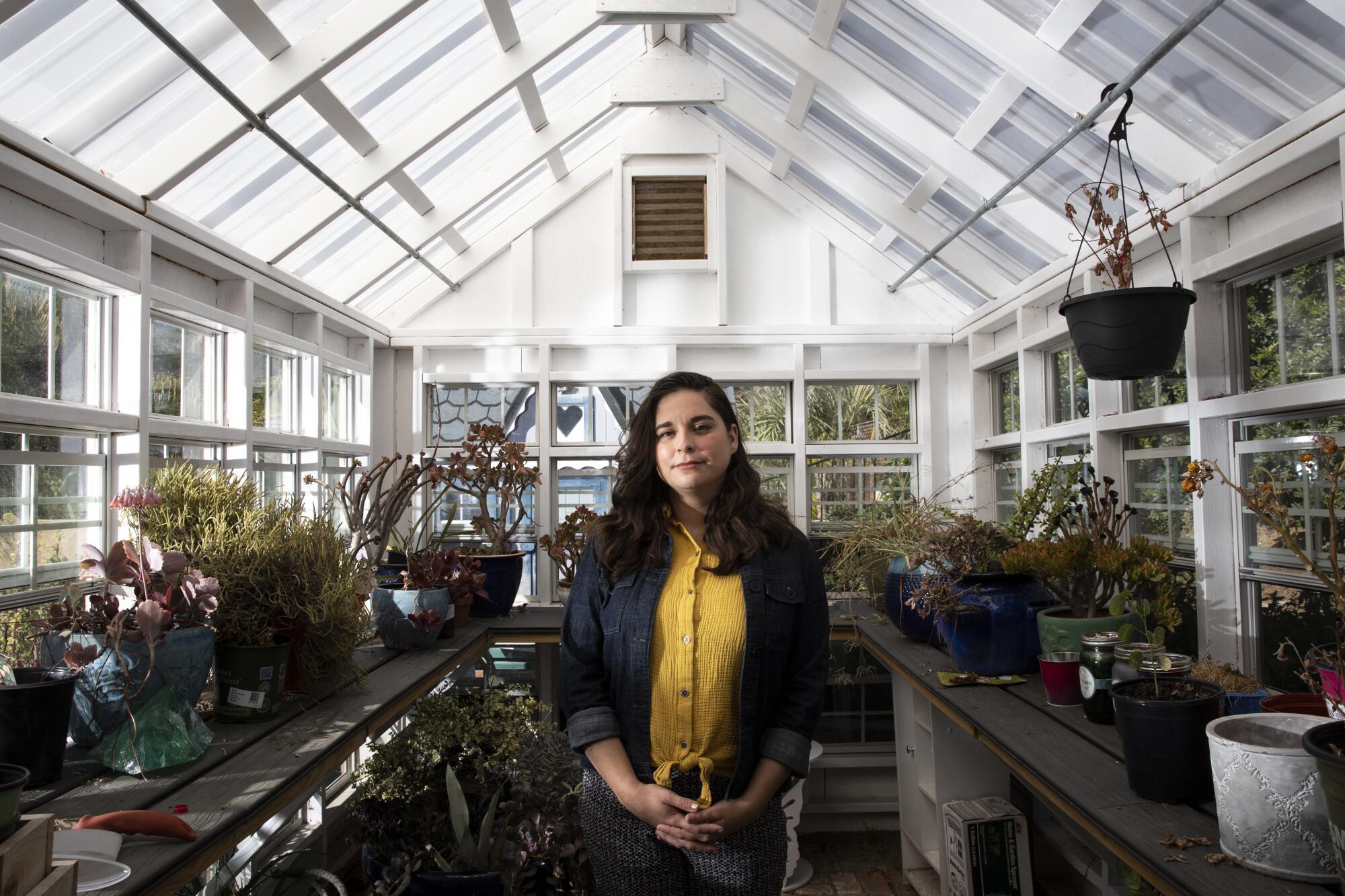 a woman stands in a greenhouse surrounded by potted plants and garden tools