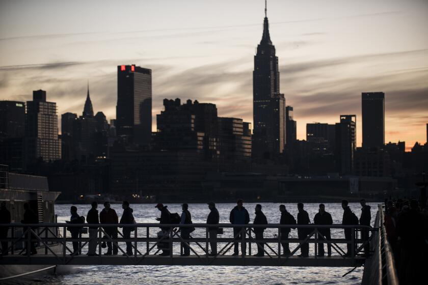People board a ferry with the Manhattan skyline in the background.