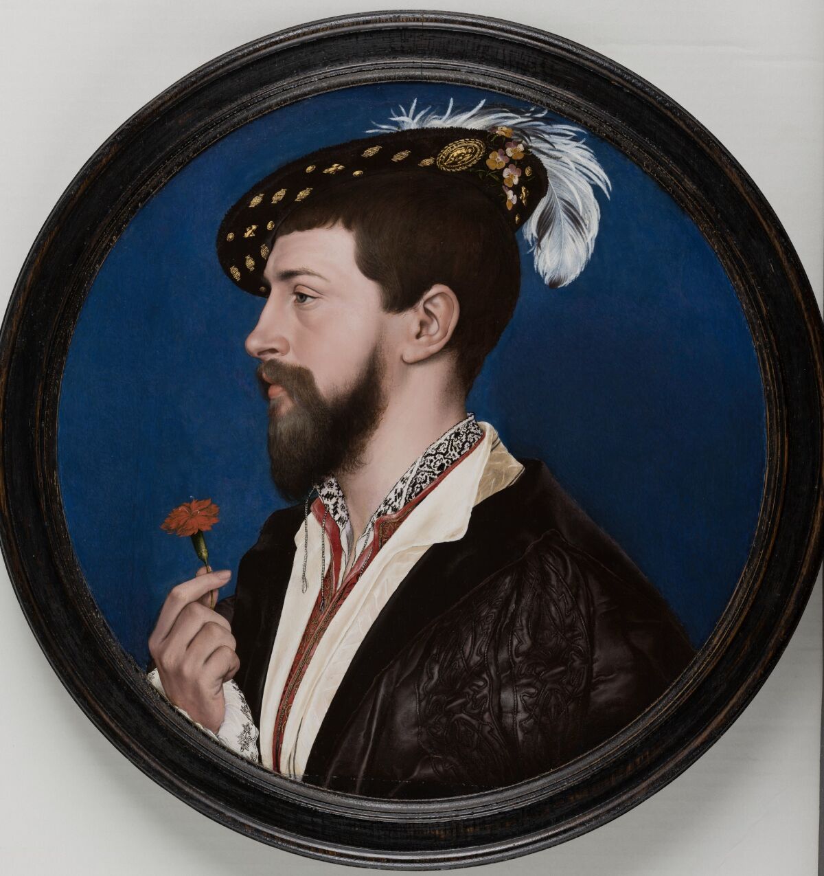 A portrait on a circular canvas shows a man in 16th century dress and a plumed hat holding a red flower.