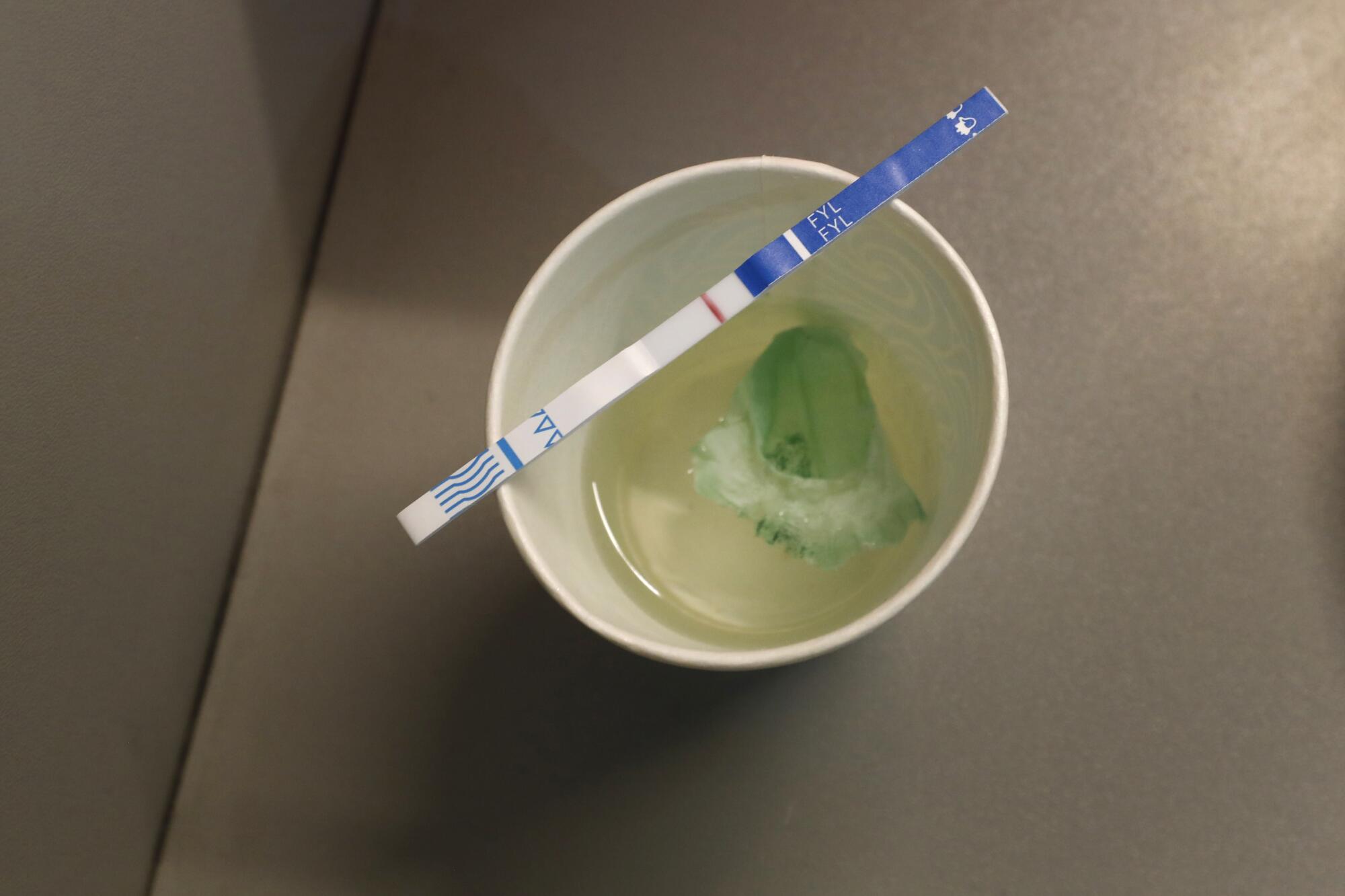 Una tira reactiva descansa sobre un vaso de líquido transparente con una sustancia verde
