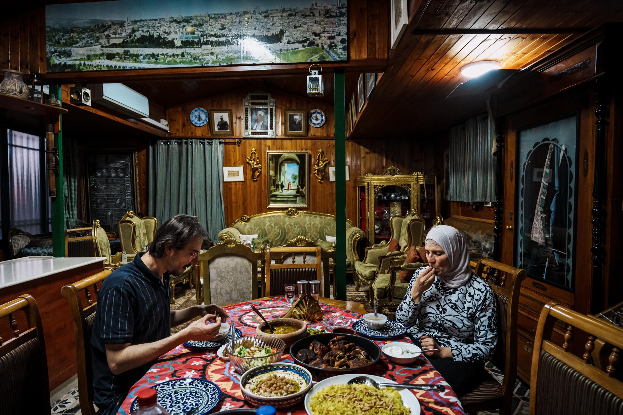 Um homem e uma mulher mais velha estão sentados à mesa de uma casa, comendo uma refeição iftar.