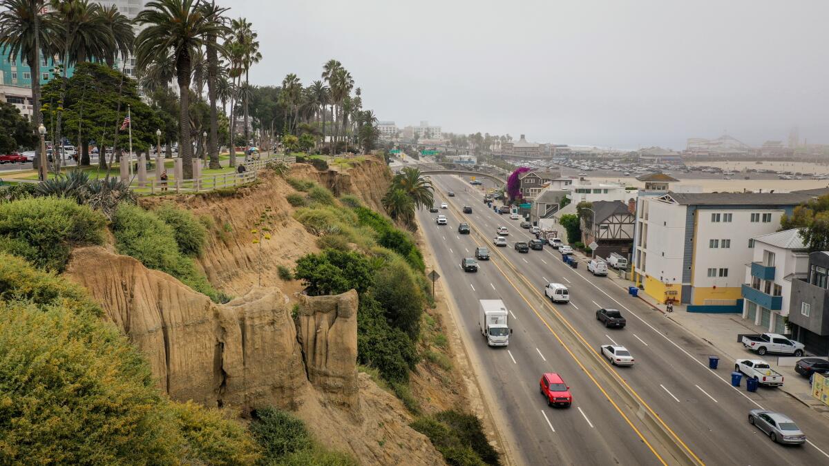 As seen from atop high bluffs, cars and trucks drive on a multi-lane road.