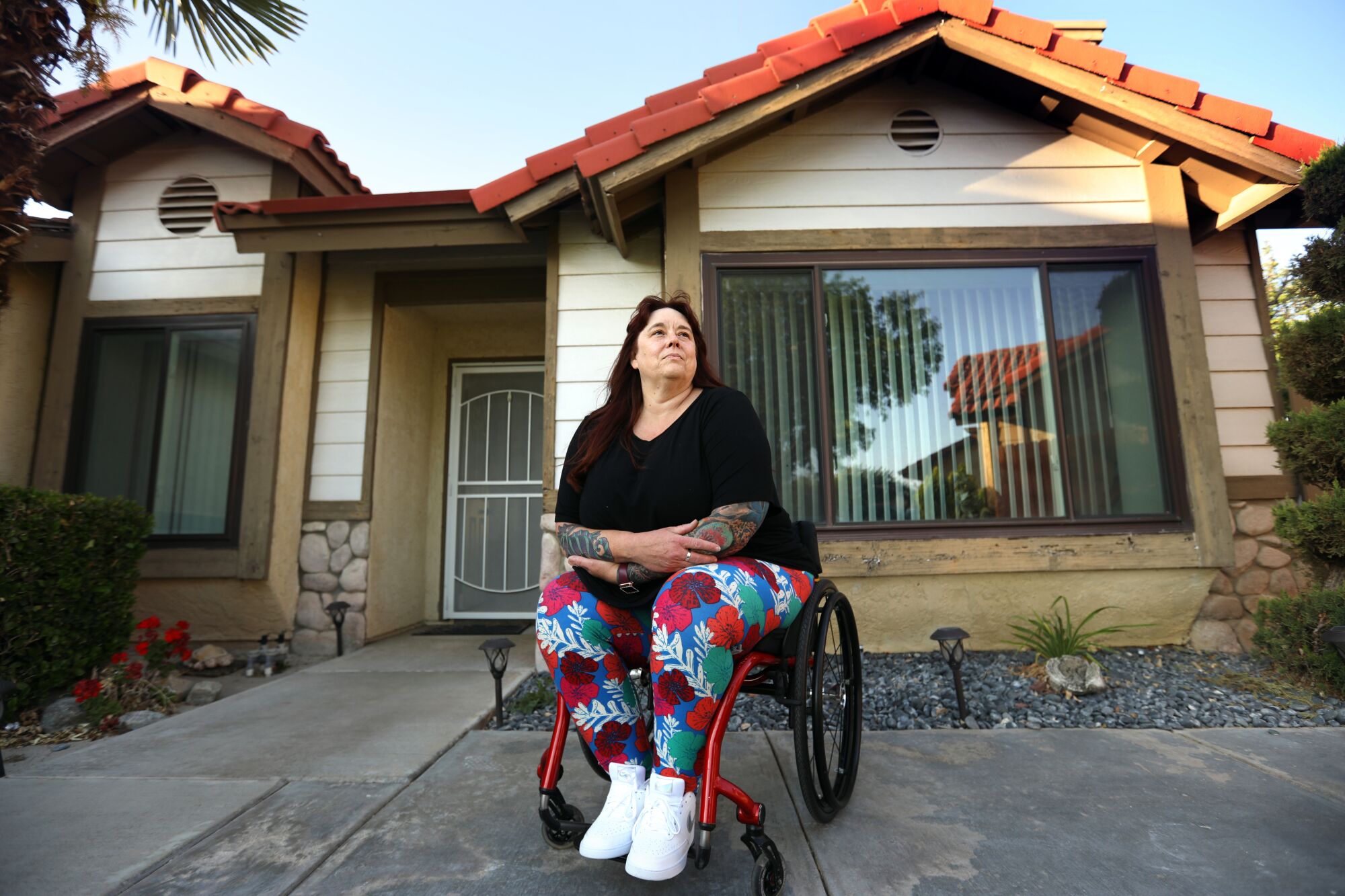 A woman sits in a wheelchair outside a house