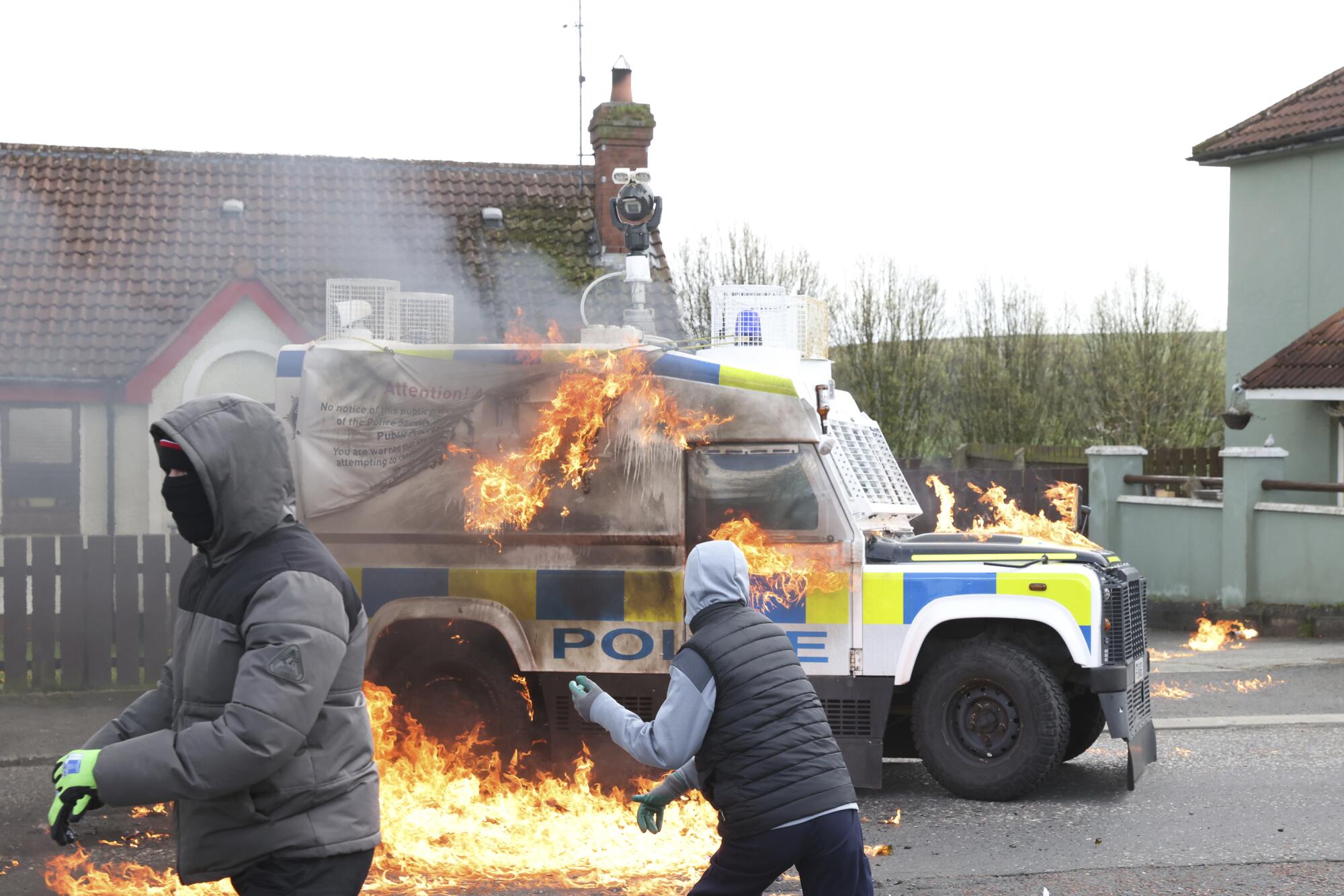 In Northern Ireland, two masked youths throw gas bombs at a police Land Rover, which is starting to burn.