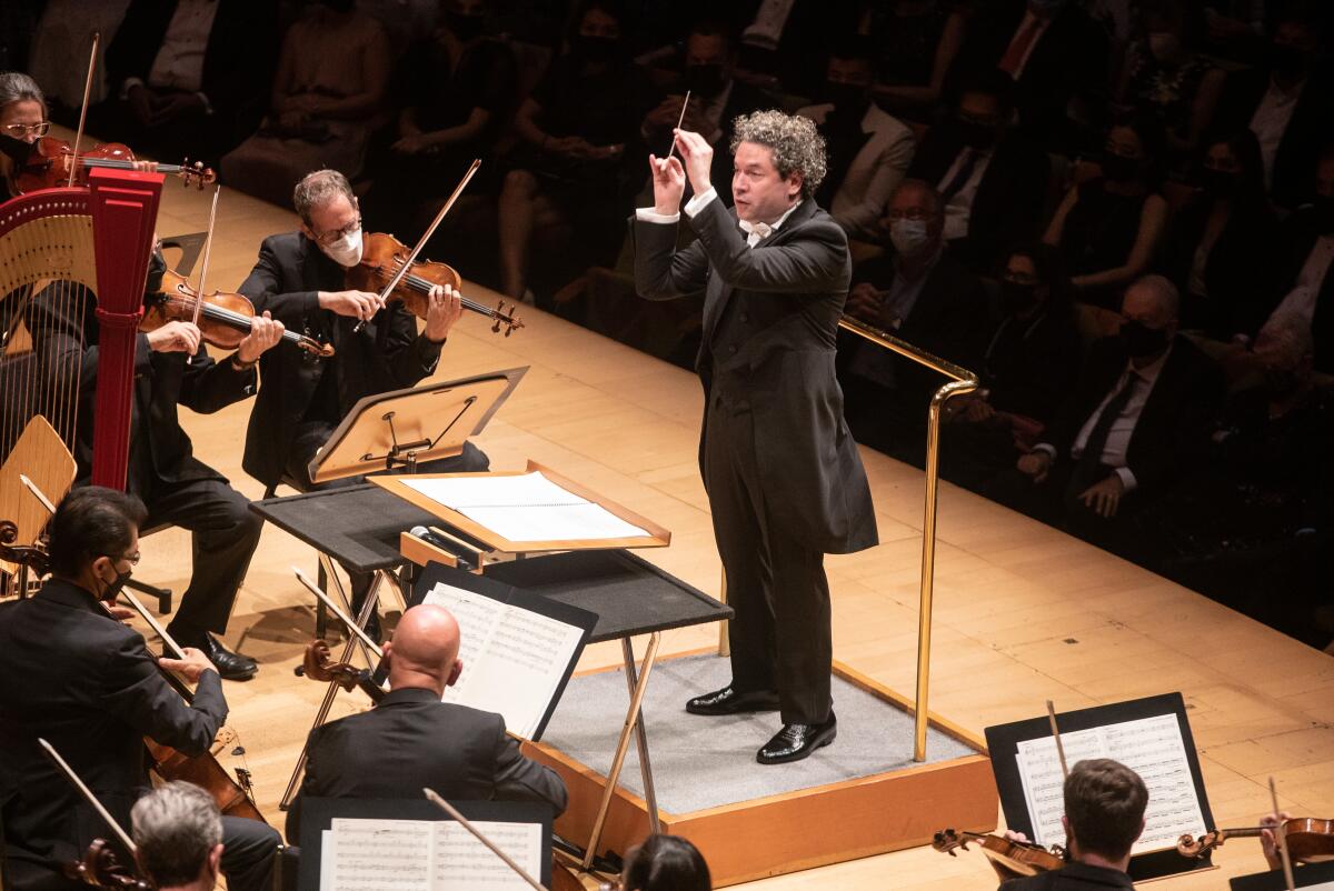 Gustavo Dudamel, with curly hair and an all-black ensemble, holds up a baton as he conducts the L.A. Phil.