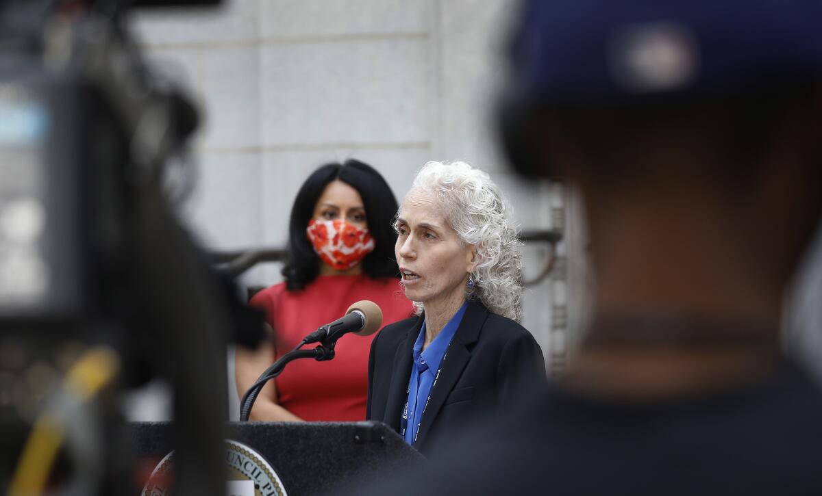 A woman speaks into a microphone at a lectern outside City Hall.