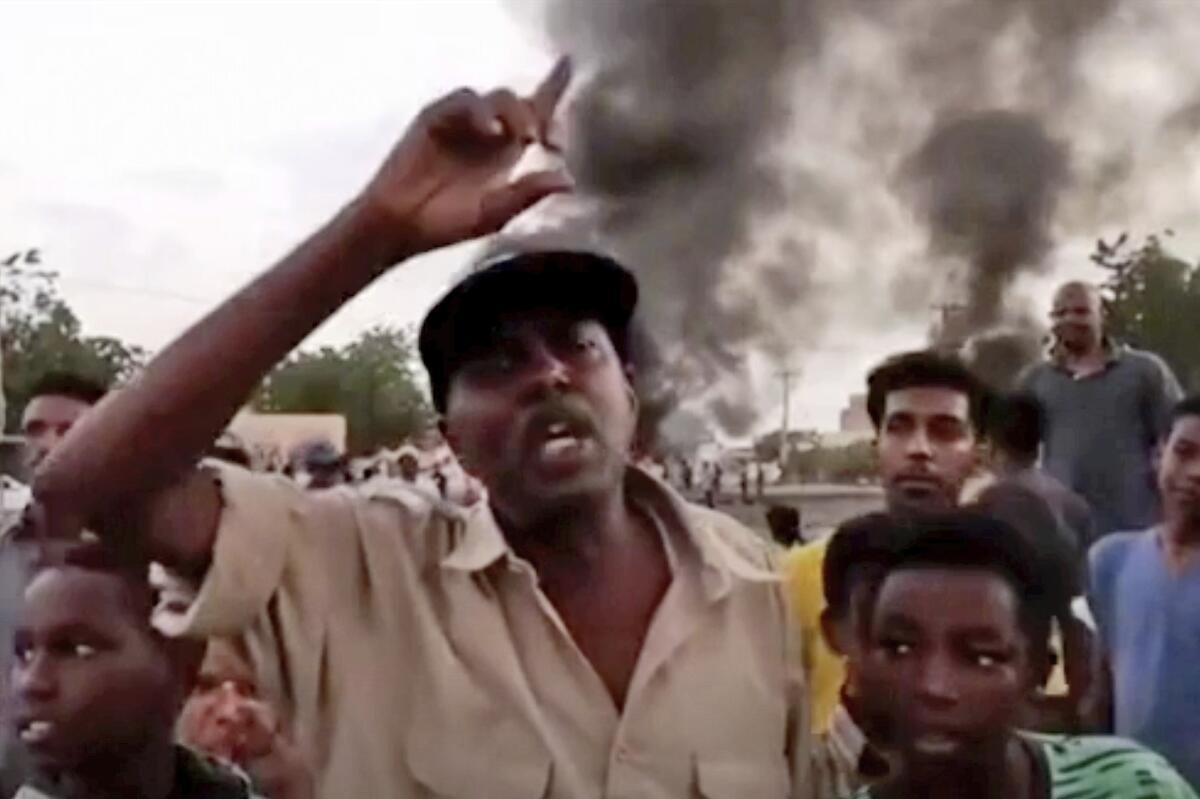 People protesting in Khartoum, Sudan, with smoke rising behind them