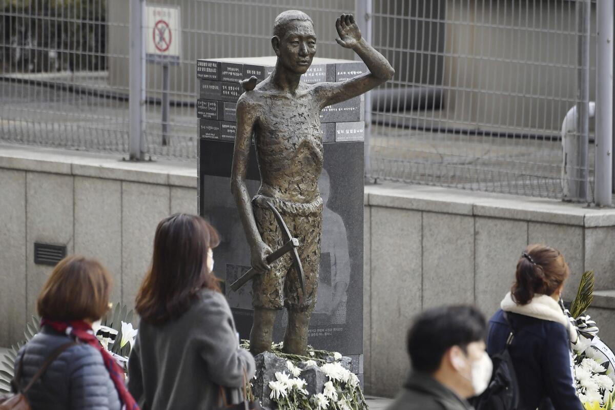 Varias personas pasan frente a una estatua que simboliza a los coreanos obligados a realizar trabajos forzados