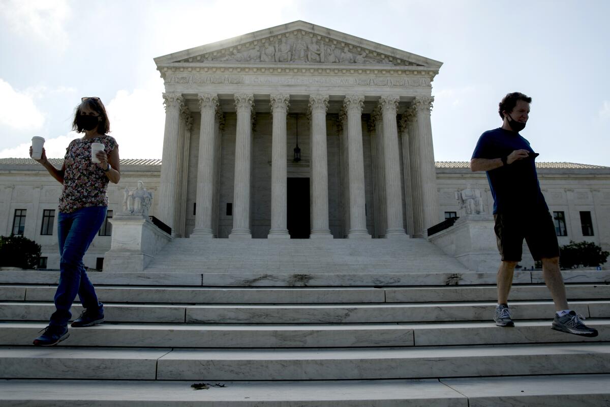 Two people wearing masks walk down the steps outside the Supreme Court.