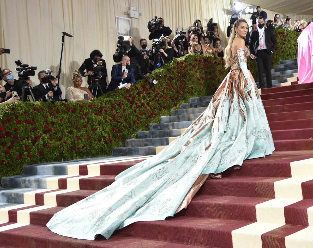 Blake Lively ascends a tall staircase wearing a dress with a long two-tone train