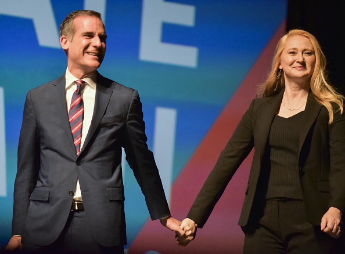 L.A. Mayor Eric Garcetti and his wife, Amy Elaine Wakeland, hold hands onstage