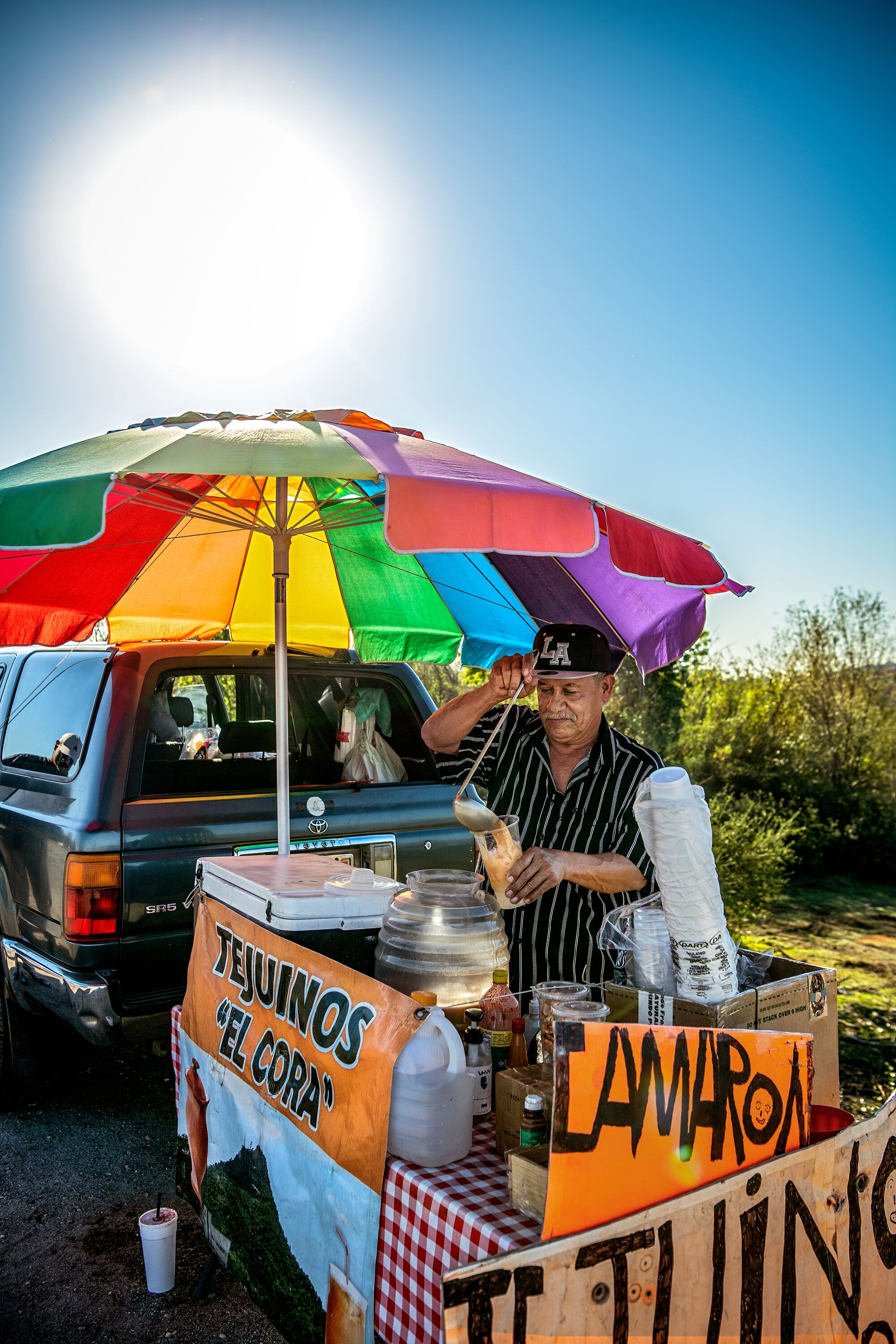 A vendor serves tejuino from a roadside stand under a colorful umbrella.