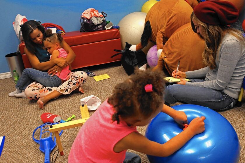 Aquah Clark holds her daughter Waniya while twin sister Haki plays during a session with occupational therapist Melissa Francis. Both girls are autistic, and their care is managed by the Inland Regional Center.