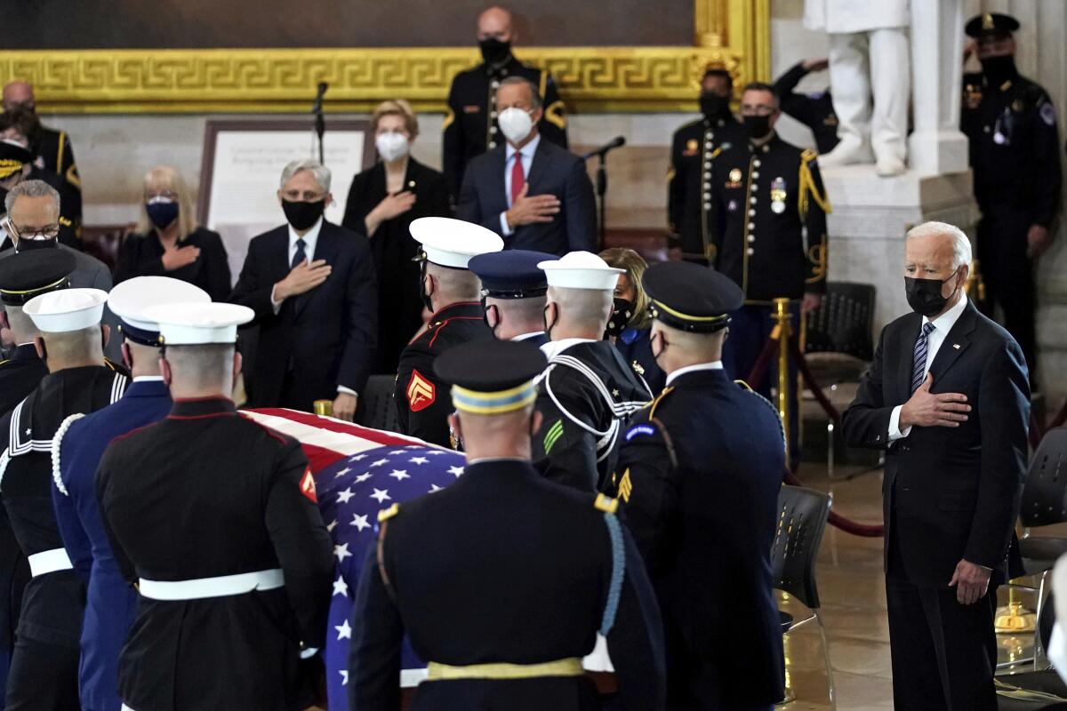 President Biden, right, stands with his hand over his heart as an honor guard carries a flag-draped casket