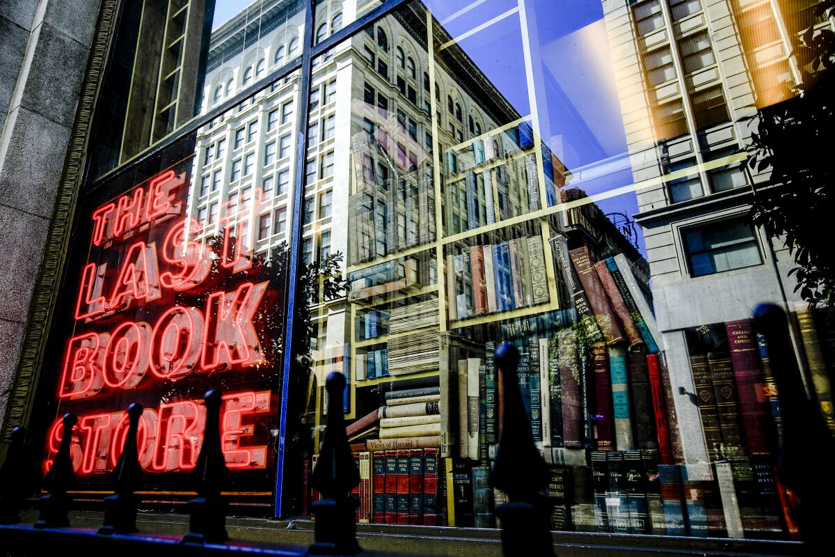 A red neon window sign reads "the Last Bookstore." Tall buildings are reflected in the window.