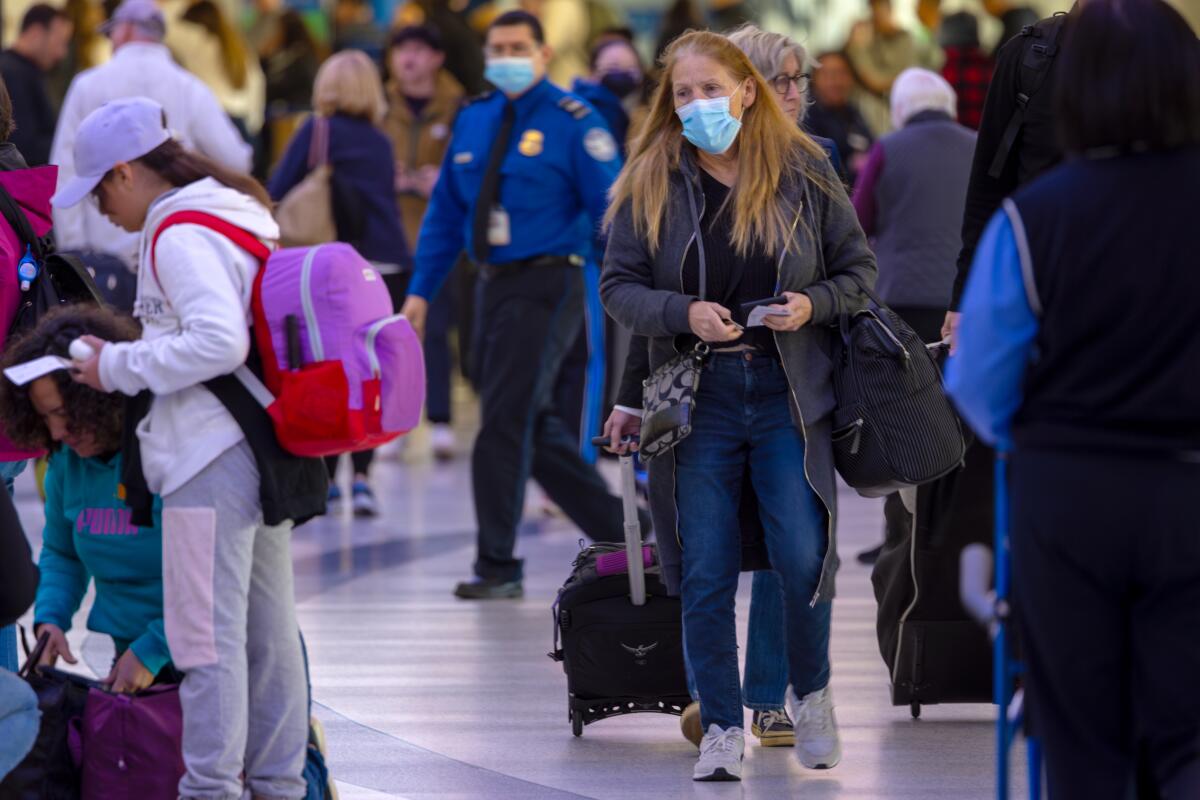 Passengers with and without face masks travel through at Los Angeles International Airport in January.