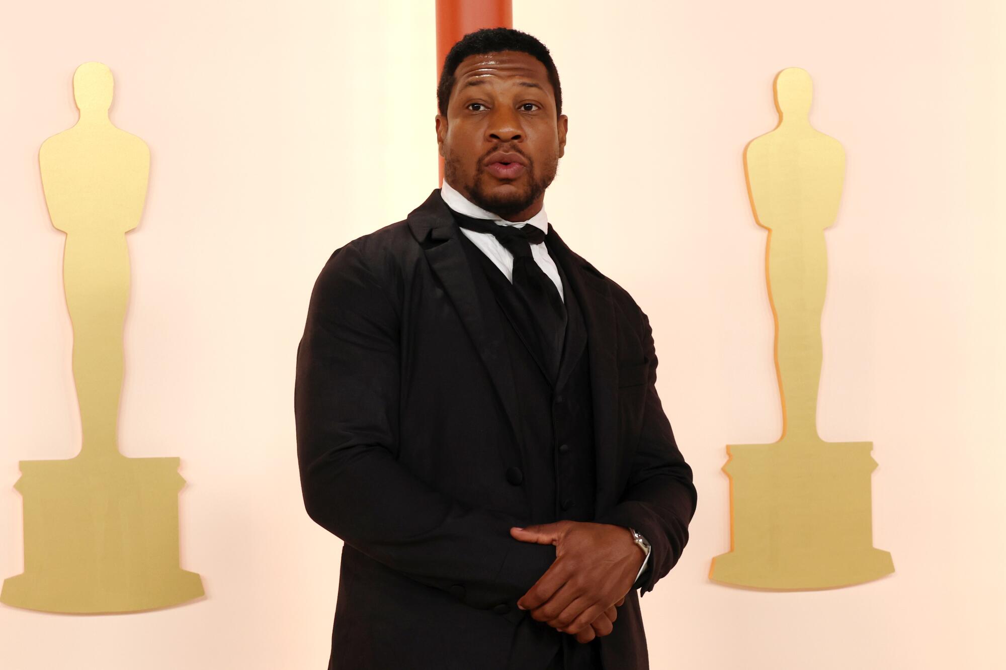 Jonathan Majors in a three-piece black suit with middle-1800s-style shirt collar and tie. 