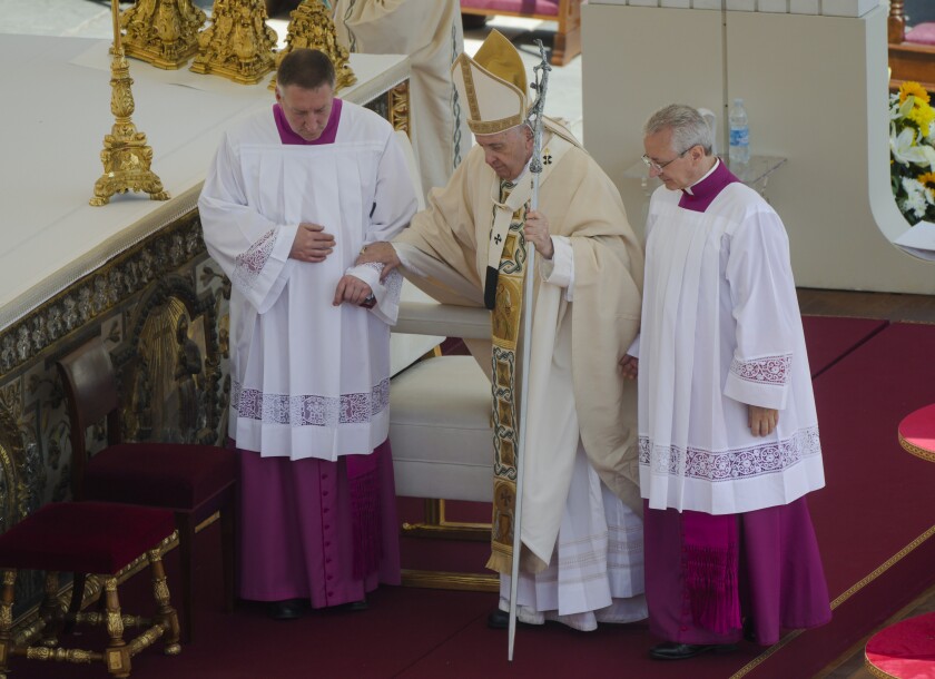 Two men in robes help support Pope Francis.