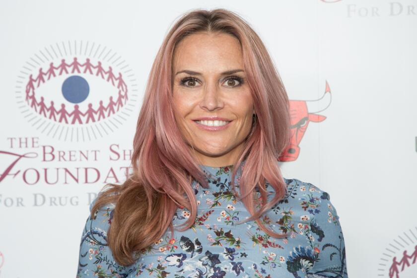 Brooke Mueller smiles with light pink highlights in her blond hair while wearing a printed high-neck top