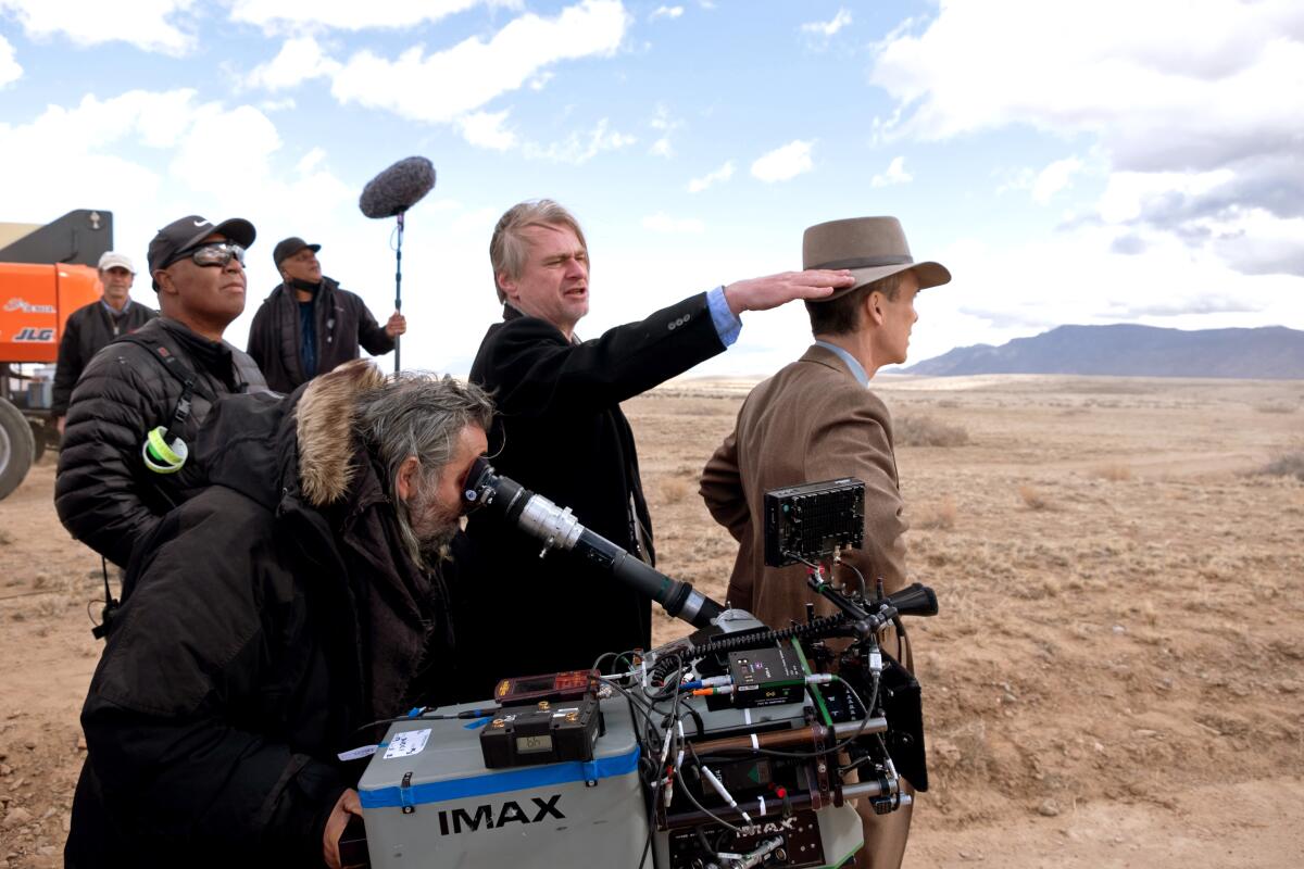 Christopher Nolan and crew stand in a dirt field with filmmaking equipment.