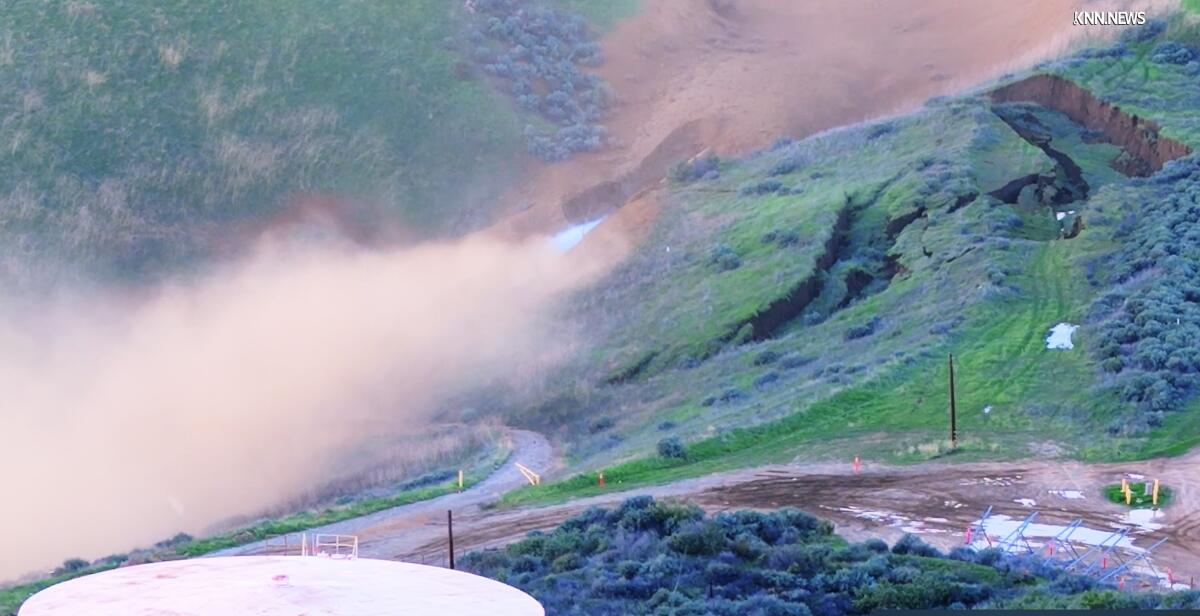 Dust rises from a hillside beside a freeway.
