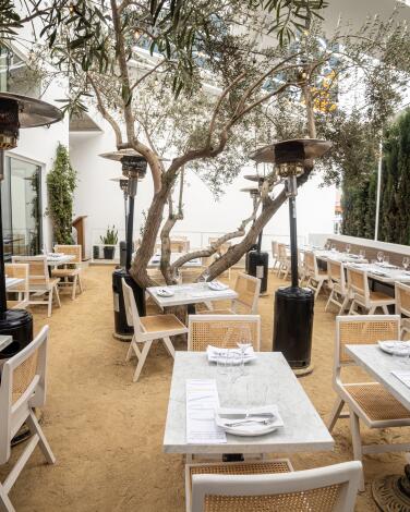 The outdoor patio area at Cento, with white tables and chairs under heat lamps and twisting cypress trees.
