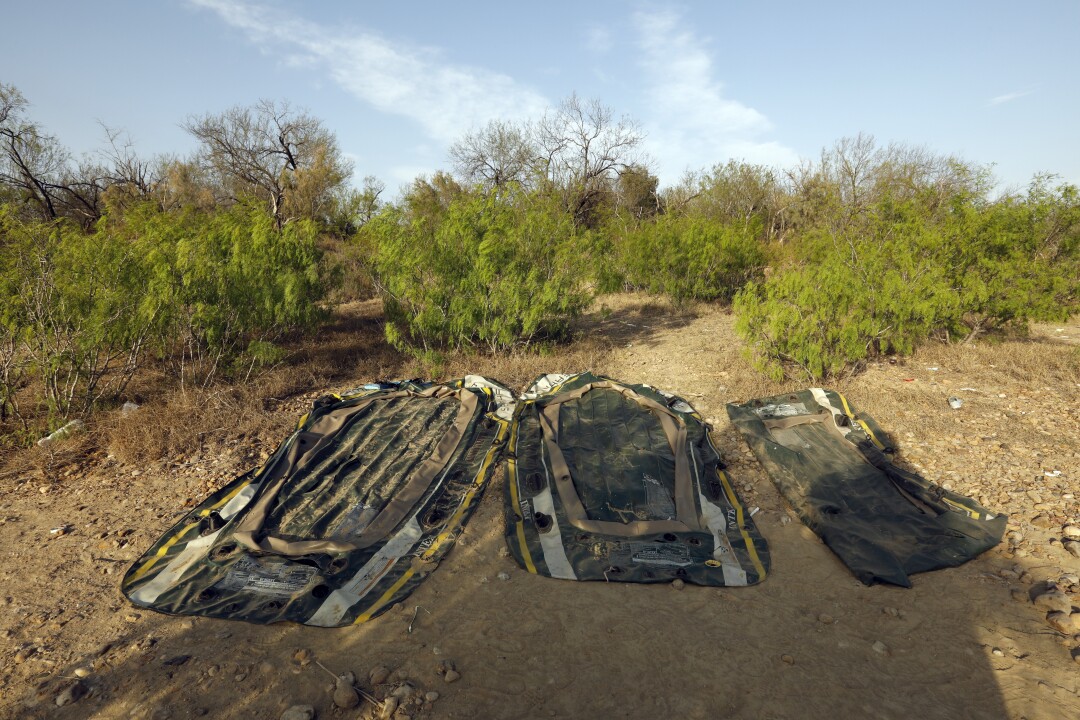 Three deflated black plastic rafts lie in the dirt.