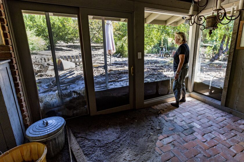 OAK GLEN, CA - SEPTEMBER 15, 2022: Resident Meg Grant stares out at mud and destruction which once was a lush patio and garden area before Monday's heavy rains breached the nearby flood channel dumping heavy mud flow and debris into her house and property on Potato Canyon Road September 15, 2022 in Oak Glen, California. Grant spent months advocating county officials to address the channel, which has flooded during other rain events. But, nothing was done. Her home and others nearby are unlivable.(Gina Ferazzi / Los Angeles Times)