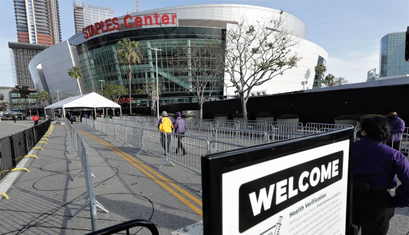 Two people walk towards the Staples Center Arena with a welcome sign in the foreground