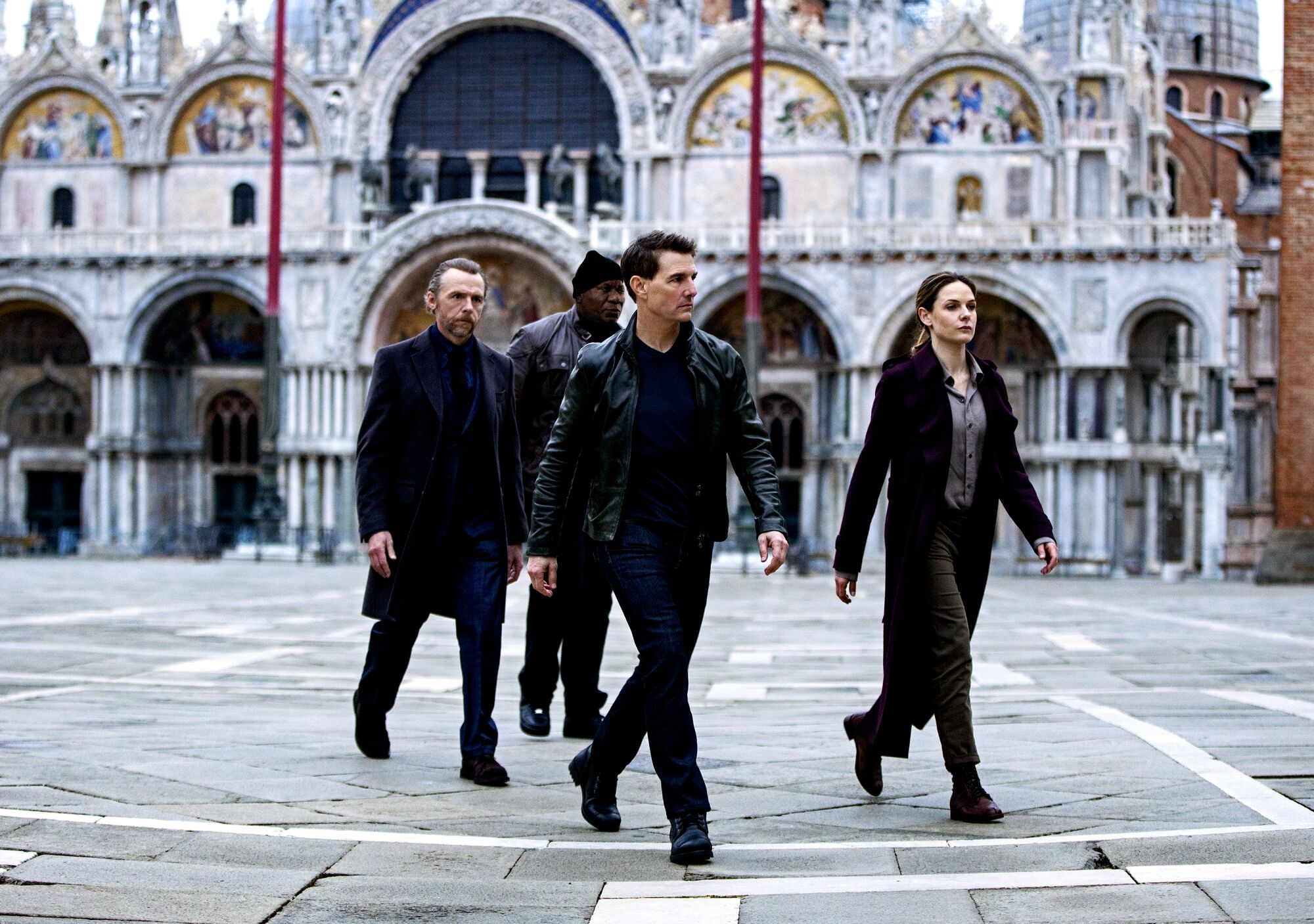 A quarter of people dressed in black walk through a square before an ornate building.