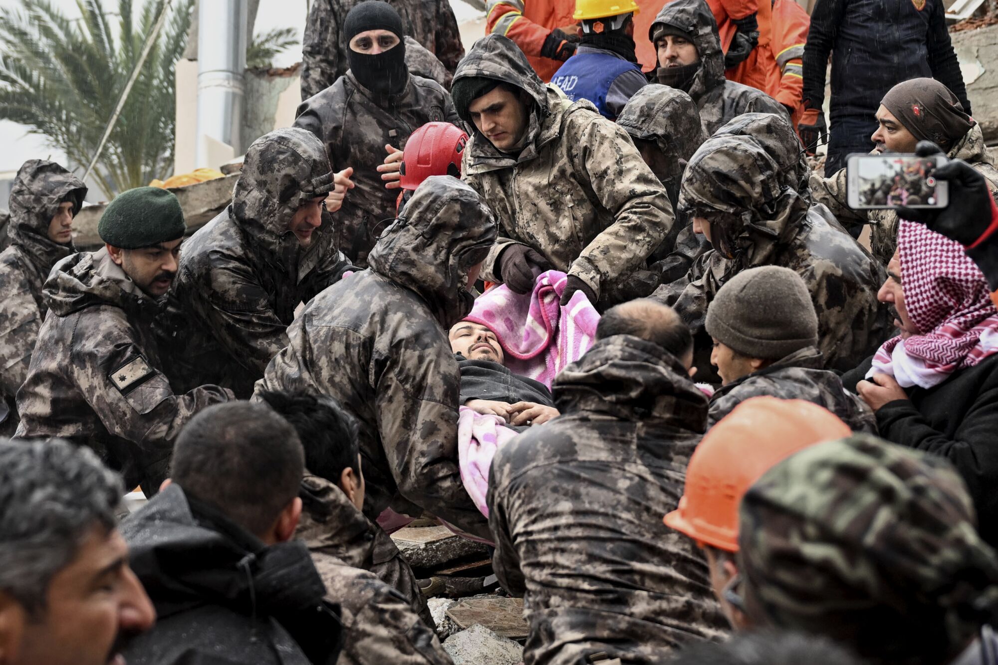 A man, wrapped in a pink blanket, is carried by a group of men in brown military camouflage jackets