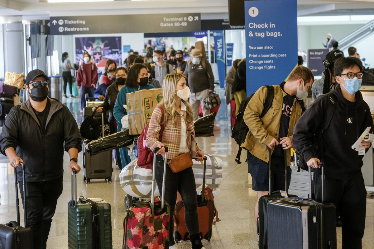 Viajeros con mascarillas hacen fila para facturar en el Aeropuerto Internacional de Los Ángeles en Los Ángeles