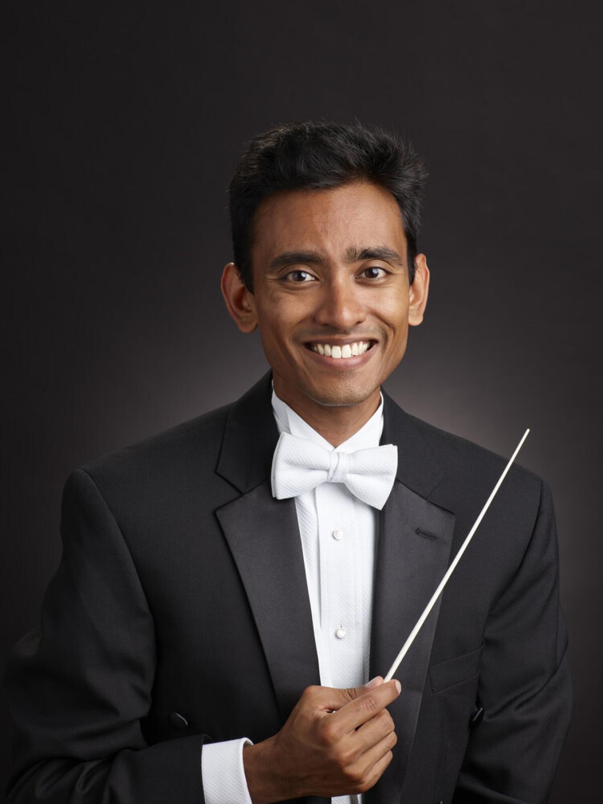 A conductor holds a baton and poses for the camera.