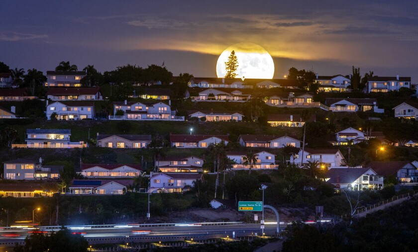 The Sturgeon Moon, the last supermoon of the year, rises above a hillside covered with homes.