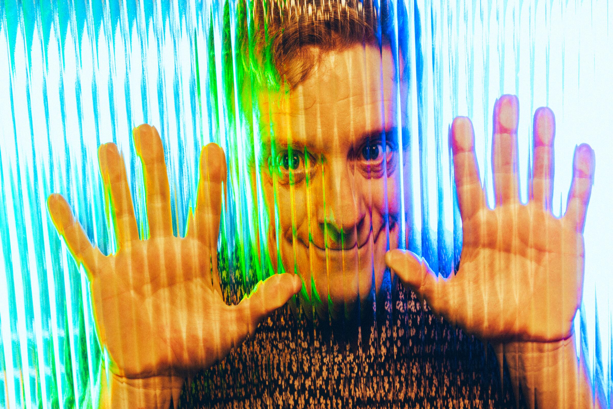Alan Tudyk presses up against rippled glass for a portrait.