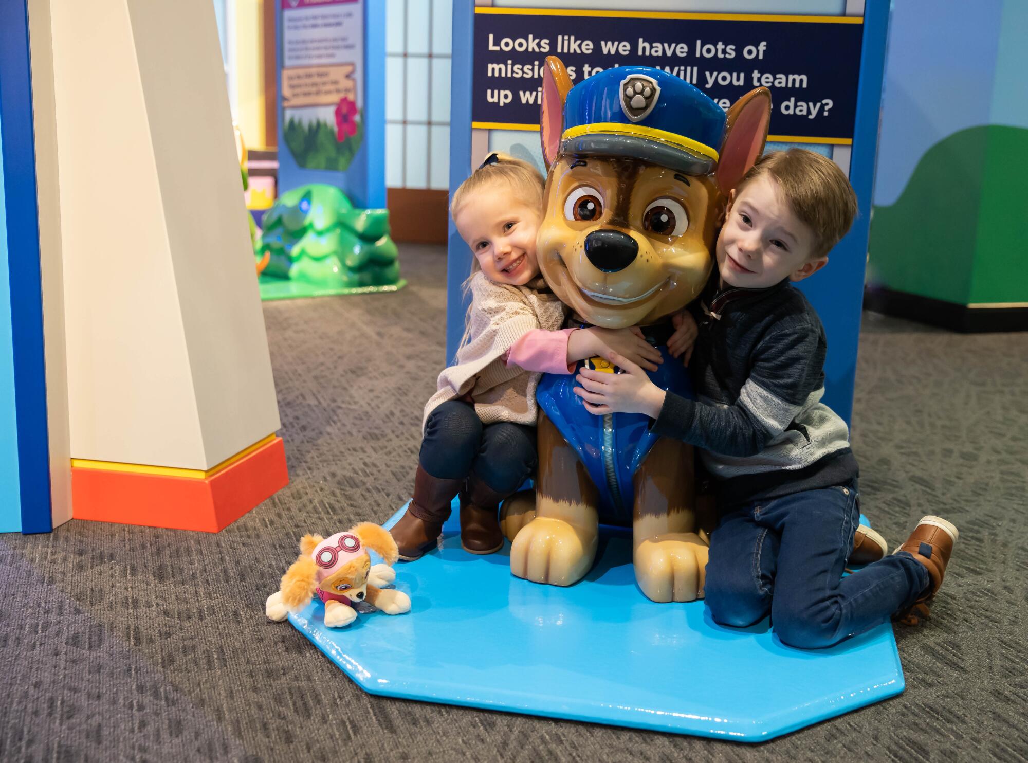 Two young children hug a small statue of a dog dressed as a police officer