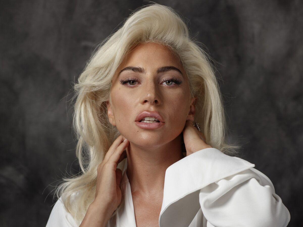 Lady Gaga poses with her mouth slightly open and her hands touching her neck.