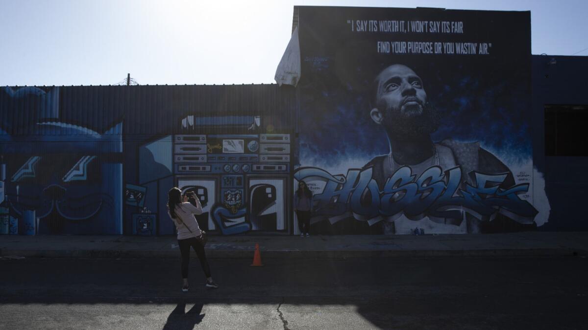 Carmen Rodriguez takes photos of artist Levi Ponce's mural of Nipsey Hussle. (Jae C. Hong / Associated Press)