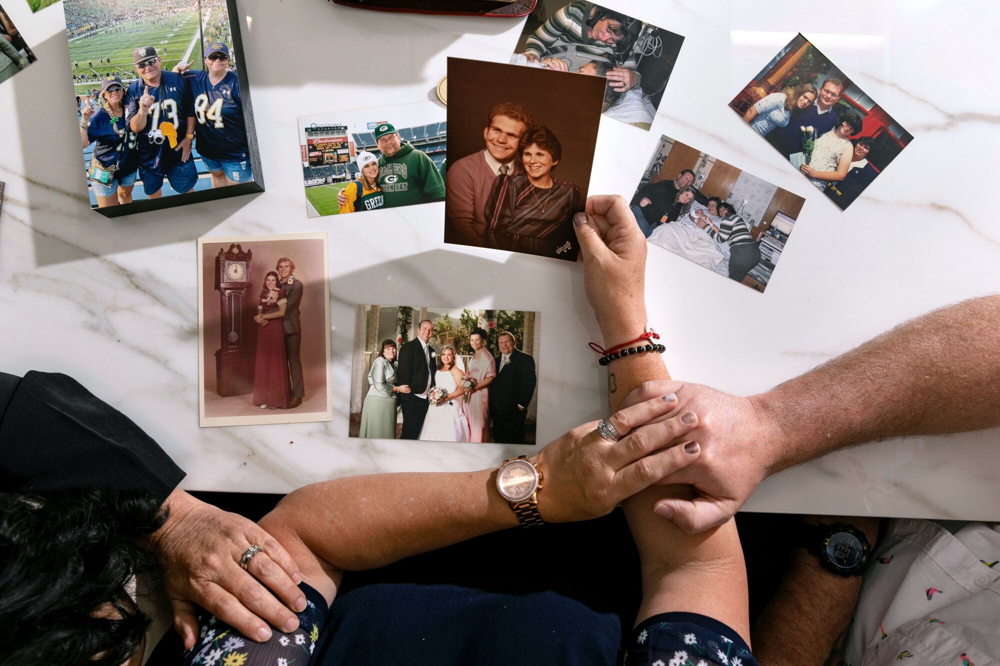 An overview of a table with family photos laid out and hands of three people resting against it, one holding a photo.