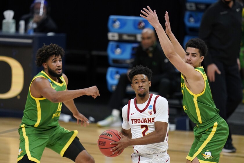 USC guard Tahj Eaddy drives between Oregon guard LJ Figueroa, left, and guard Will Richardson.