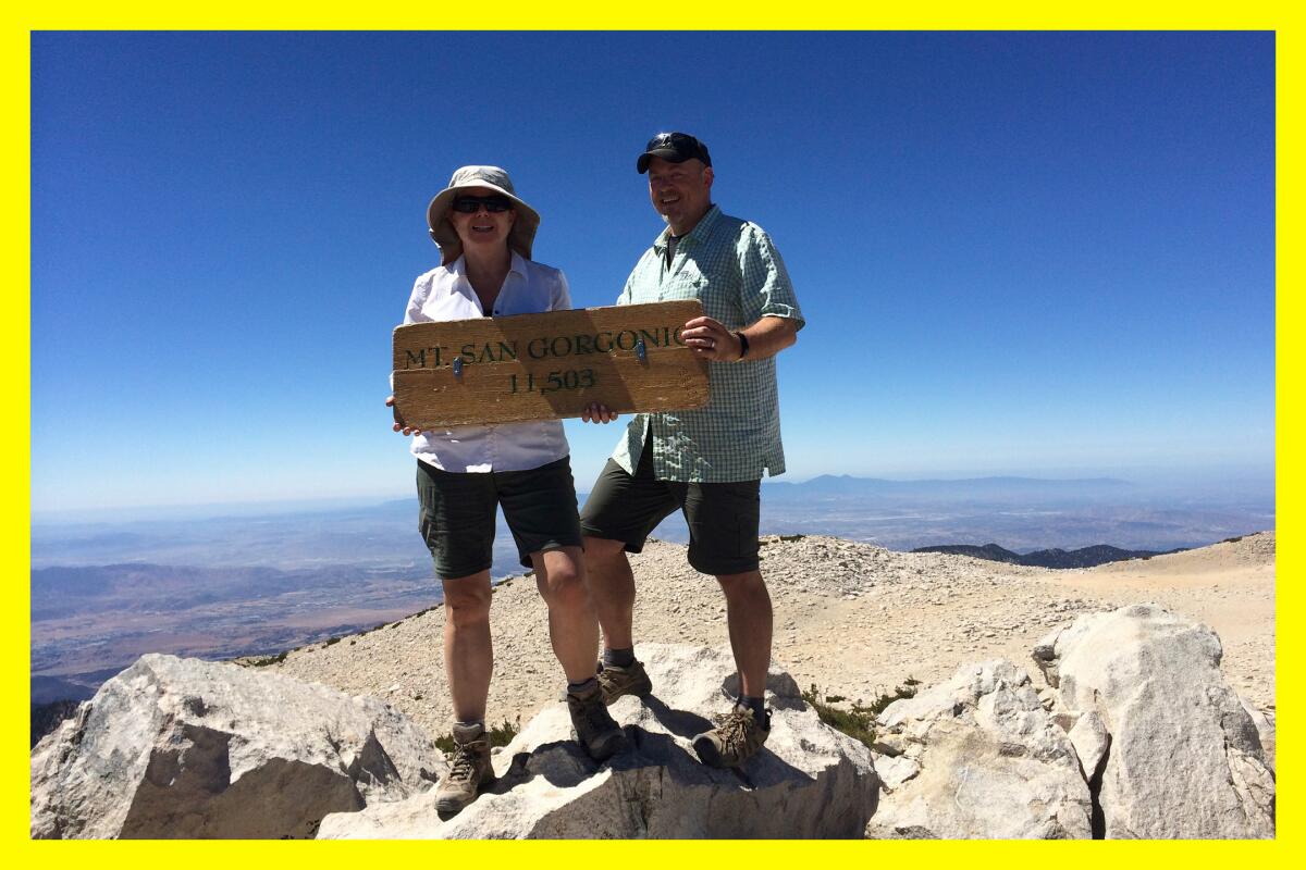 A woman and a man hold a sign that says: "Mt. San Gorgonio 11,503." Blue skies and a flatlands stretch out behind them.